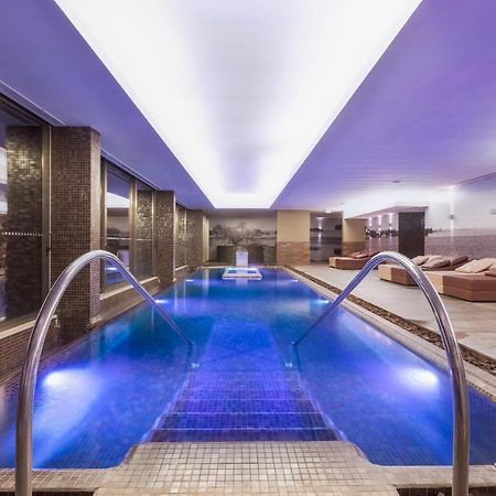 Ap Lago Montargil - Conference & Spa Buitenkant foto The photo shows a modern indoor swimming pool area. The pool features a sleek design with steps leading into the water and a gentle curve at the sides. The water is illuminated in a blue hue, enhancing the relaxing atmosphere. Surrounding the pool ar