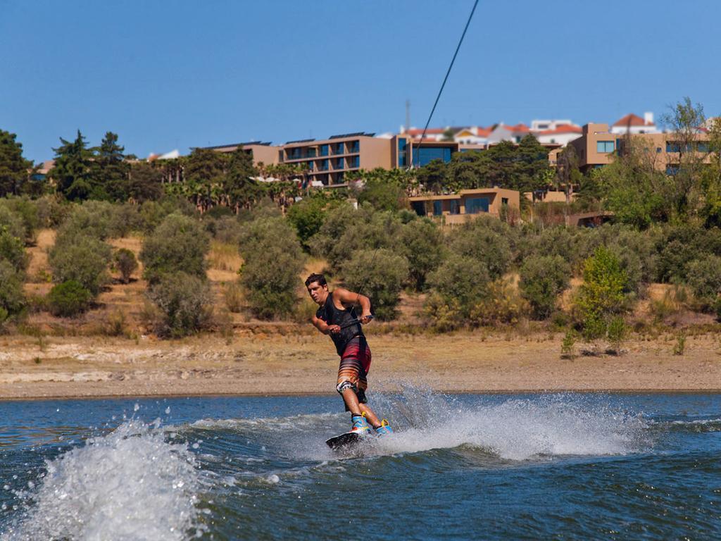 Ap Lago Montargil - Conference & Spa Buitenkant foto The photo shows a person wakeboarding on a body of water. The individual is being pulled by a cable, which is likely connected to a boat or a winch. The person is wearing a life jacket and swim shorts, balancing on the board as they enjoy the activit
