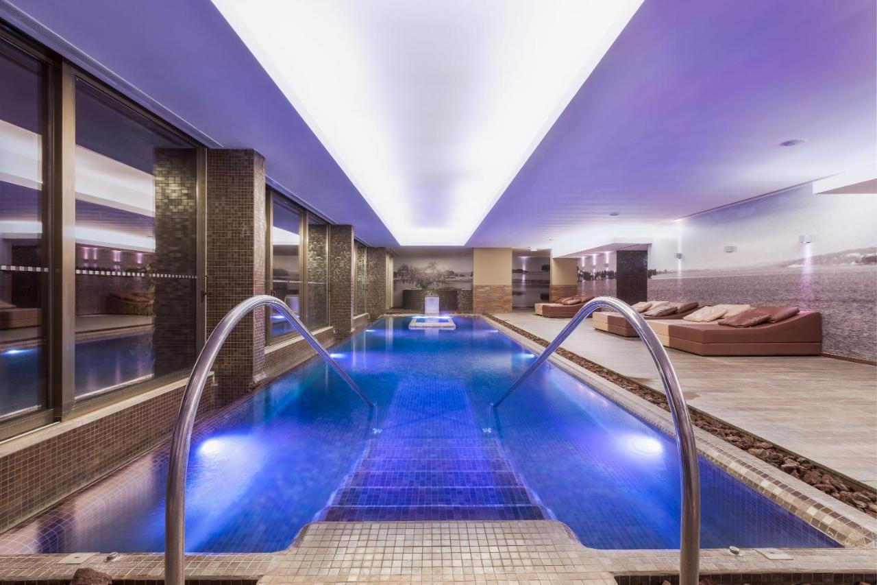 Ap Lago Montargil - Conference & Spa Buitenkant foto The photo shows a modern indoor swimming pool area. The pool features a sleek design with steps leading into the water and a gentle curve at the sides. The water is illuminated in a blue hue, enhancing the relaxing atmosphere. Surrounding the pool ar