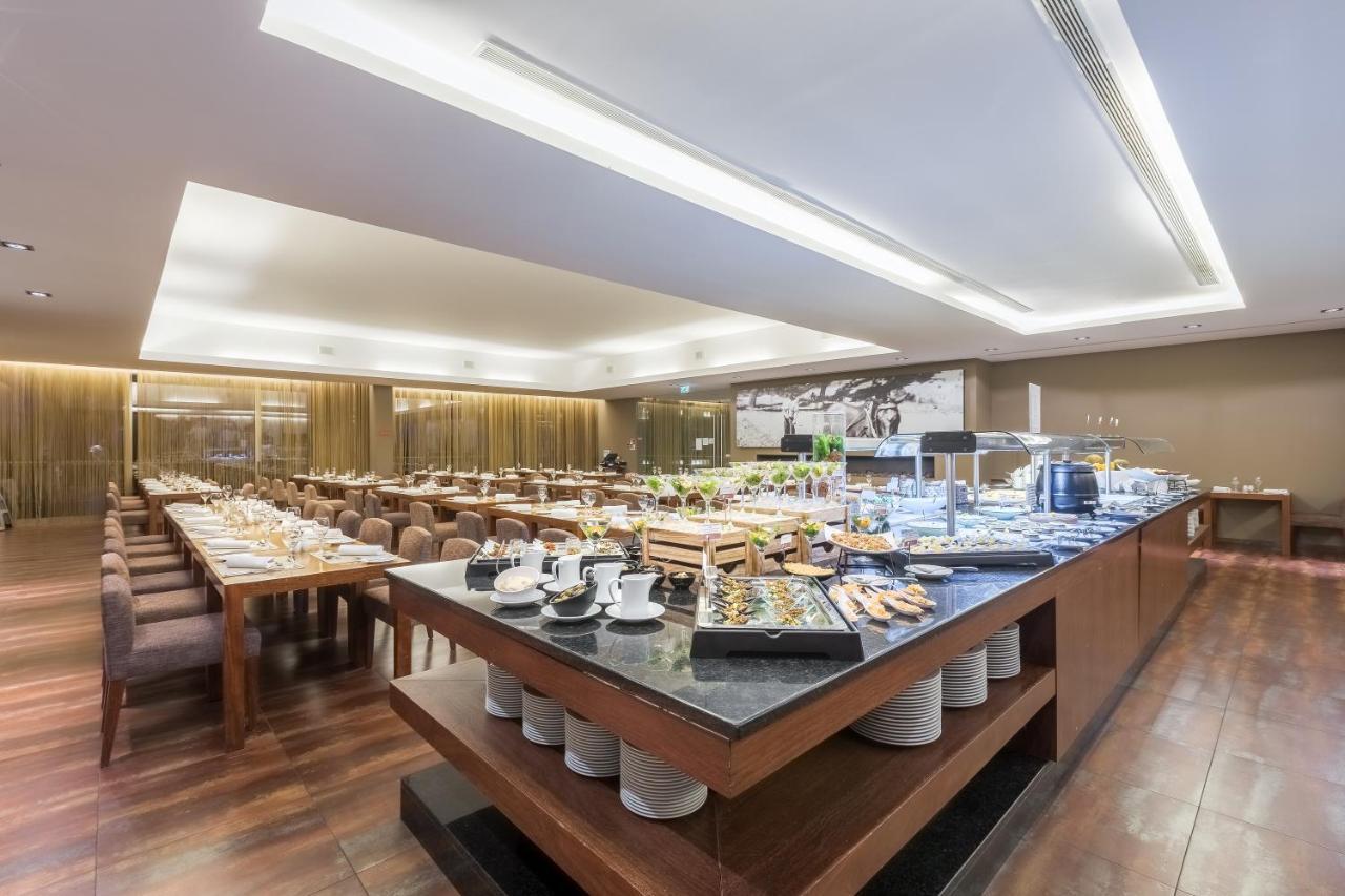 Ap Lago Montargil - Conference & Spa Buitenkant foto The photo displays a spacious restaurant interior, featuring a well-organized dining area with multiple tables set for patrons. In the center, there is a large buffet station filled with an array of food items. The decor is modern and elegant, with w