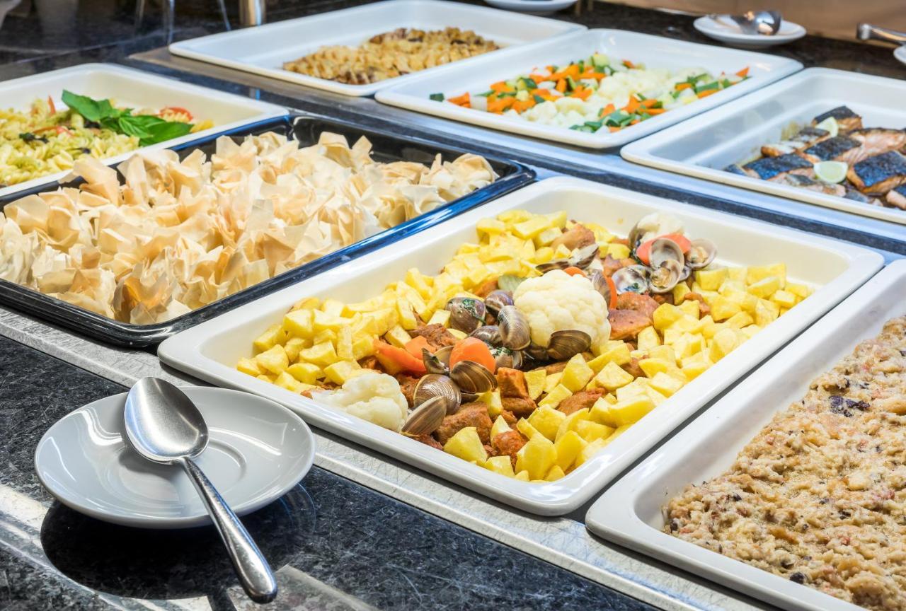 Ap Lago Montargil - Conference & Spa Buitenkant foto The photo shows a buffet-style display of various dishes. There are several rectangular trays filled with different types of food. 

1. One tray contains a mix of vegetables and seafood, likely including potatoes and cauliflower.
2. Another tray hold
