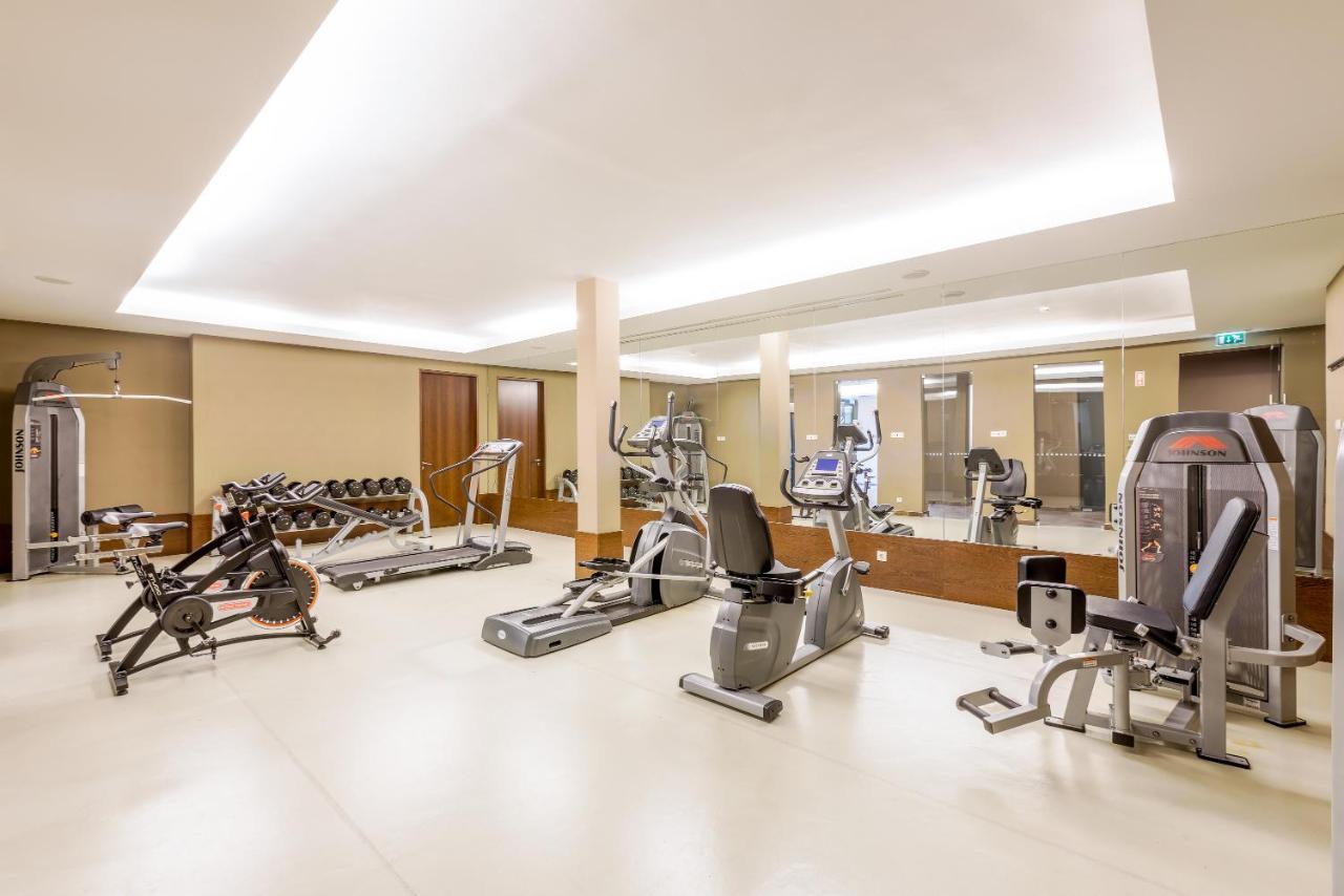 Ap Lago Montargil - Conference & Spa Buitenkant foto The image shows a modern gym interior featuring various exercise equipment. On the left, there are free weights and weight benches. In the center, there are multiple machines, including a stationary bike and an elliptical. The space is well-lit with 
