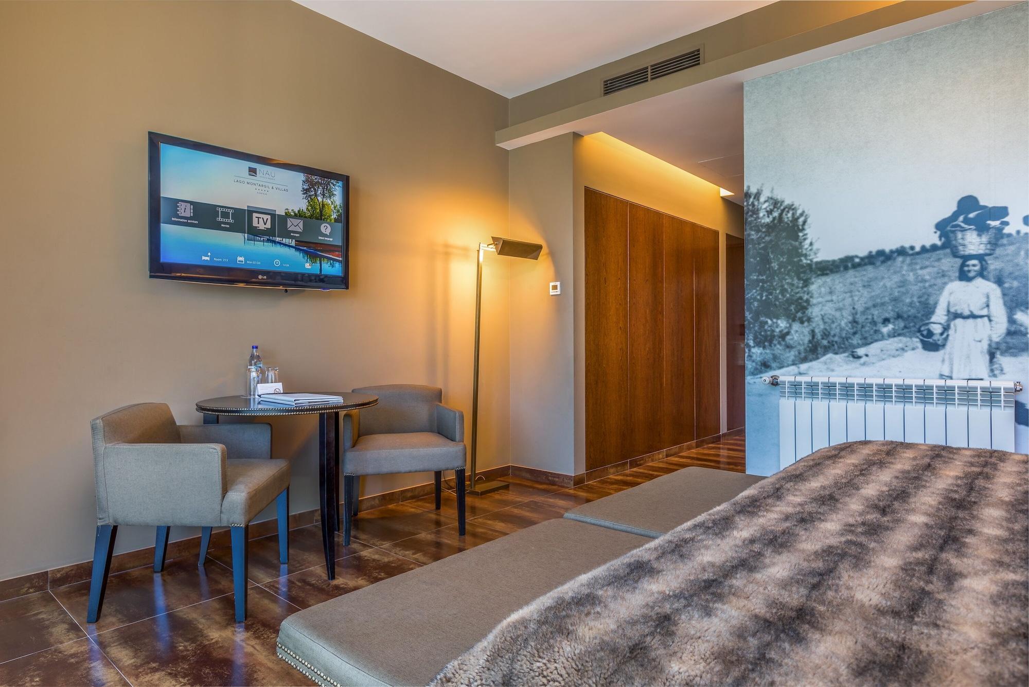 Ap Lago Montargil - Conference & Spa Buitenkant foto The photo shows an interior of a room, likely a hotel or a modern living space. In the foreground, there is a bed with a textured brown blanket. To one side, there are two comfortable chairs and a small table, possibly with a bottle of water. A flat-