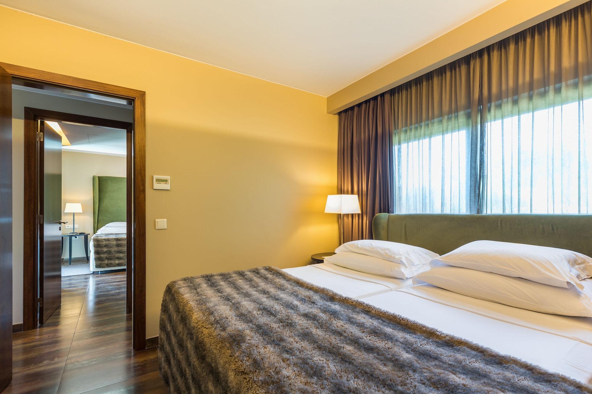 Ap Lago Montargil - Conference & Spa Buitenkant foto The photo shows the interior of a well-furnished hotel room. It features two beds with white linens and a gray decorative throw on top. The walls are painted a warm yellow, and there are floor-to-ceiling windows covered with dark curtains that allow 