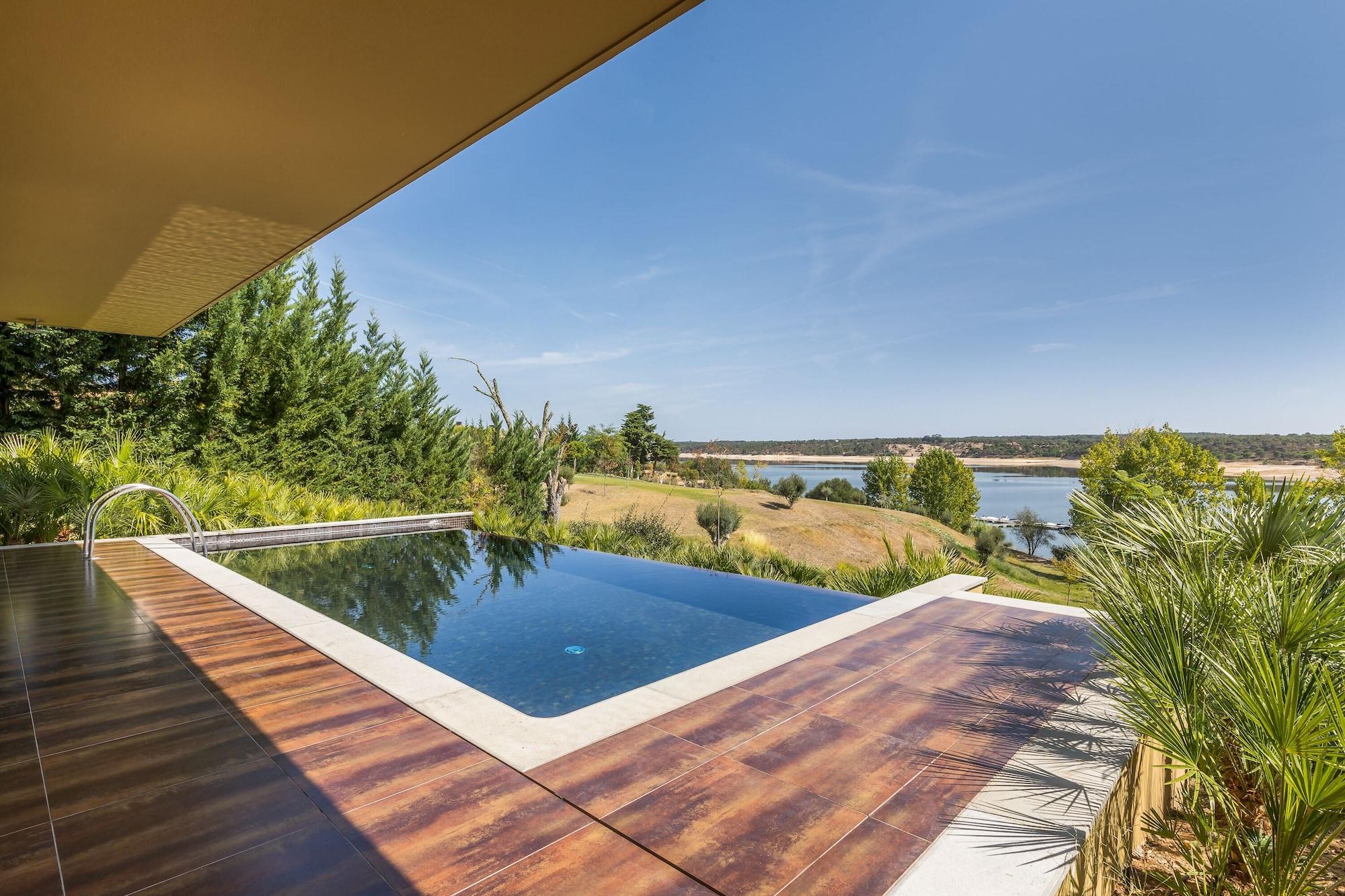 Ap Lago Montargil - Conference & Spa Buitenkant foto The photo shows a luxurious infinity pool situated on a terrace or deck. The pool features a sleek, modern design with a dark blue surface that reflects the surrounding scenery. In the background, there is a landscape of rolling hills and a body of w