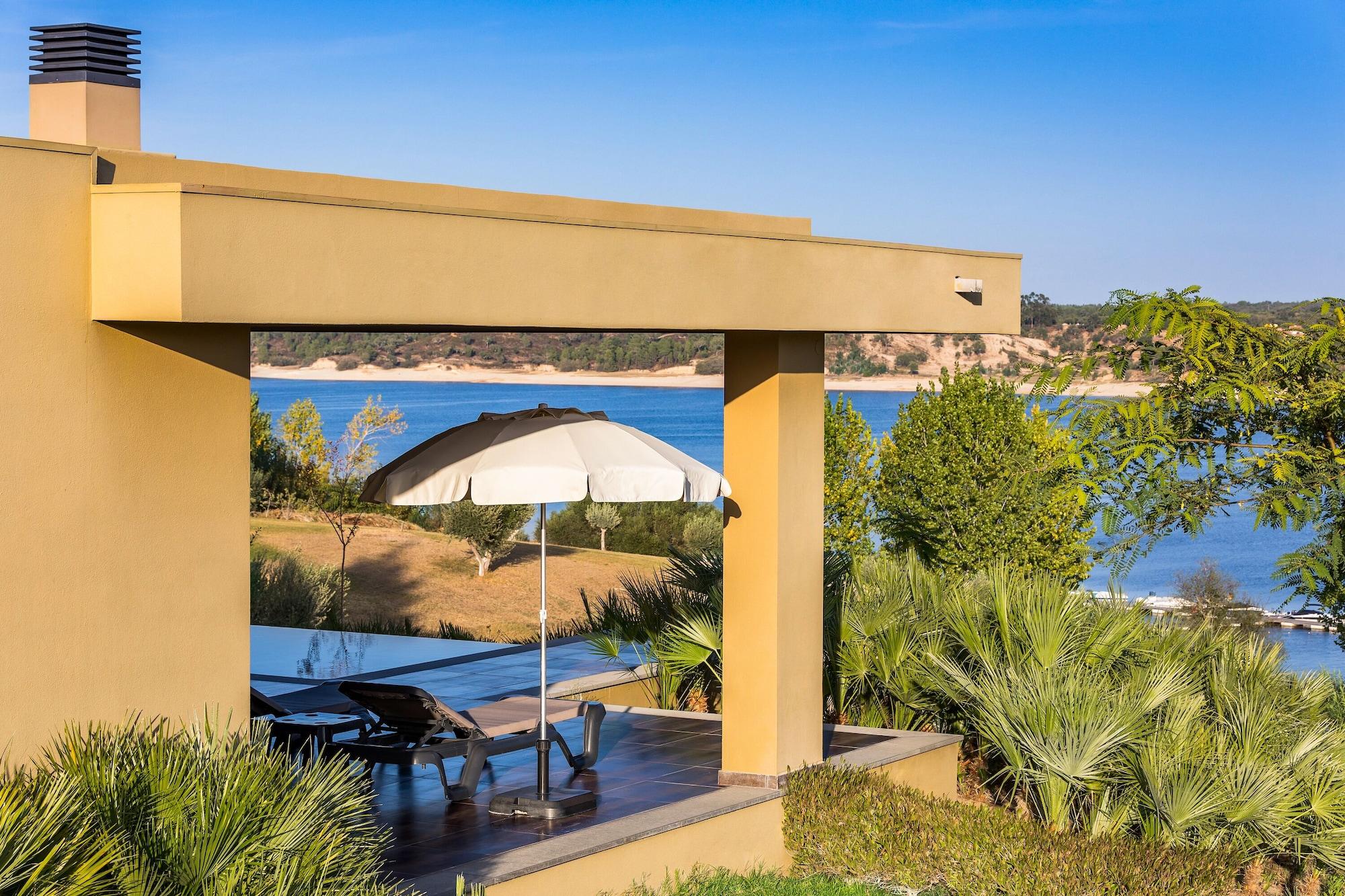 Ap Lago Montargil - Conference & Spa Buitenkant foto The photo shows a peaceful outdoor area with a modern architectural structure featuring an overhang. There is a lounge chair positioned beneath a large umbrella, creating a shaded spot to relax. In the background, there is a picturesque view of a bod