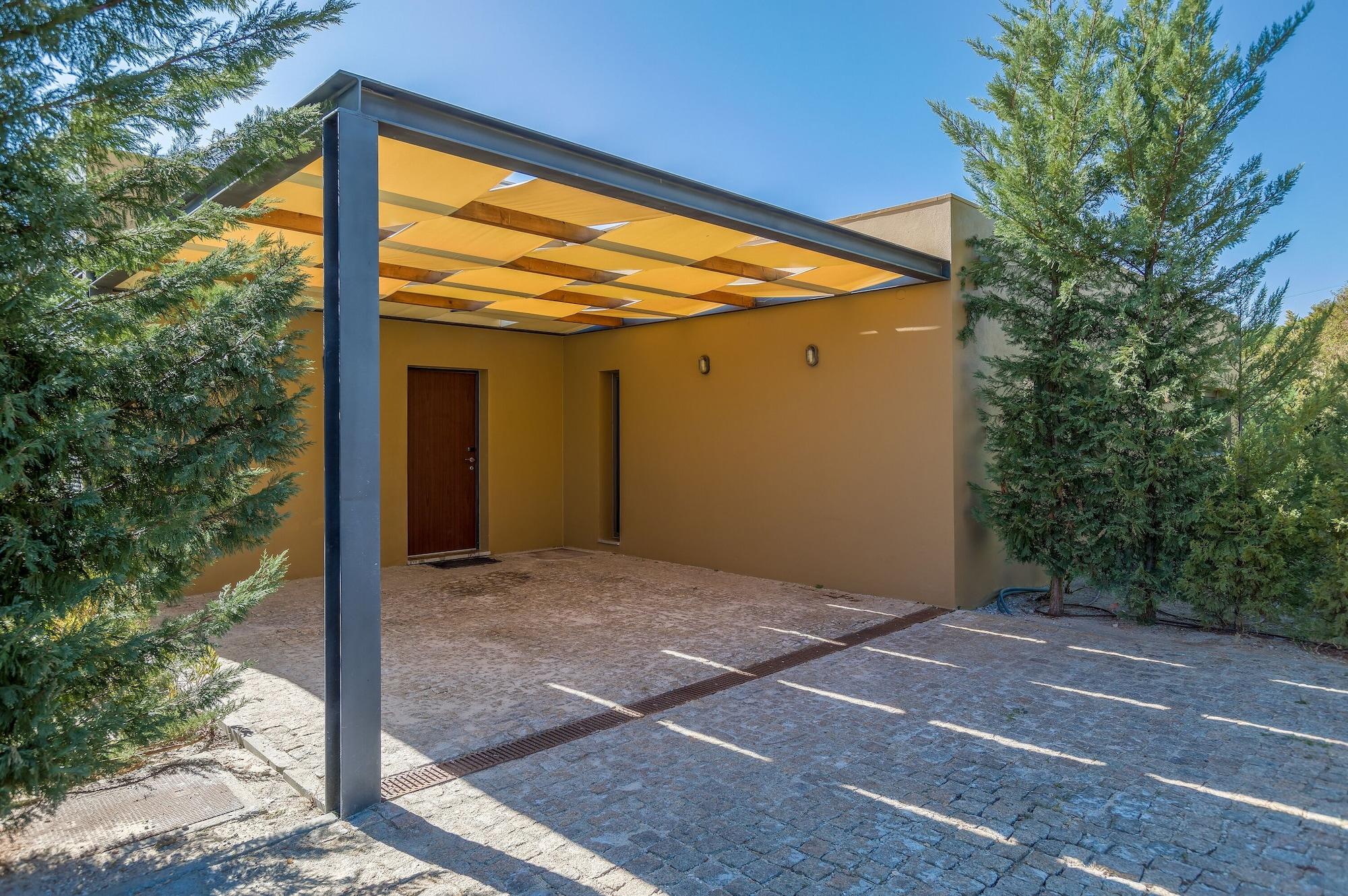 Ap Lago Montargil - Conference & Spa Buitenkant foto The photo shows an exterior view of a modern structure with a carport. The carport has a sleek, metallic frame and a yellowish canopy above it. In front of the structure, there is a paved area made of stone or tiles. The main entrance features a wood