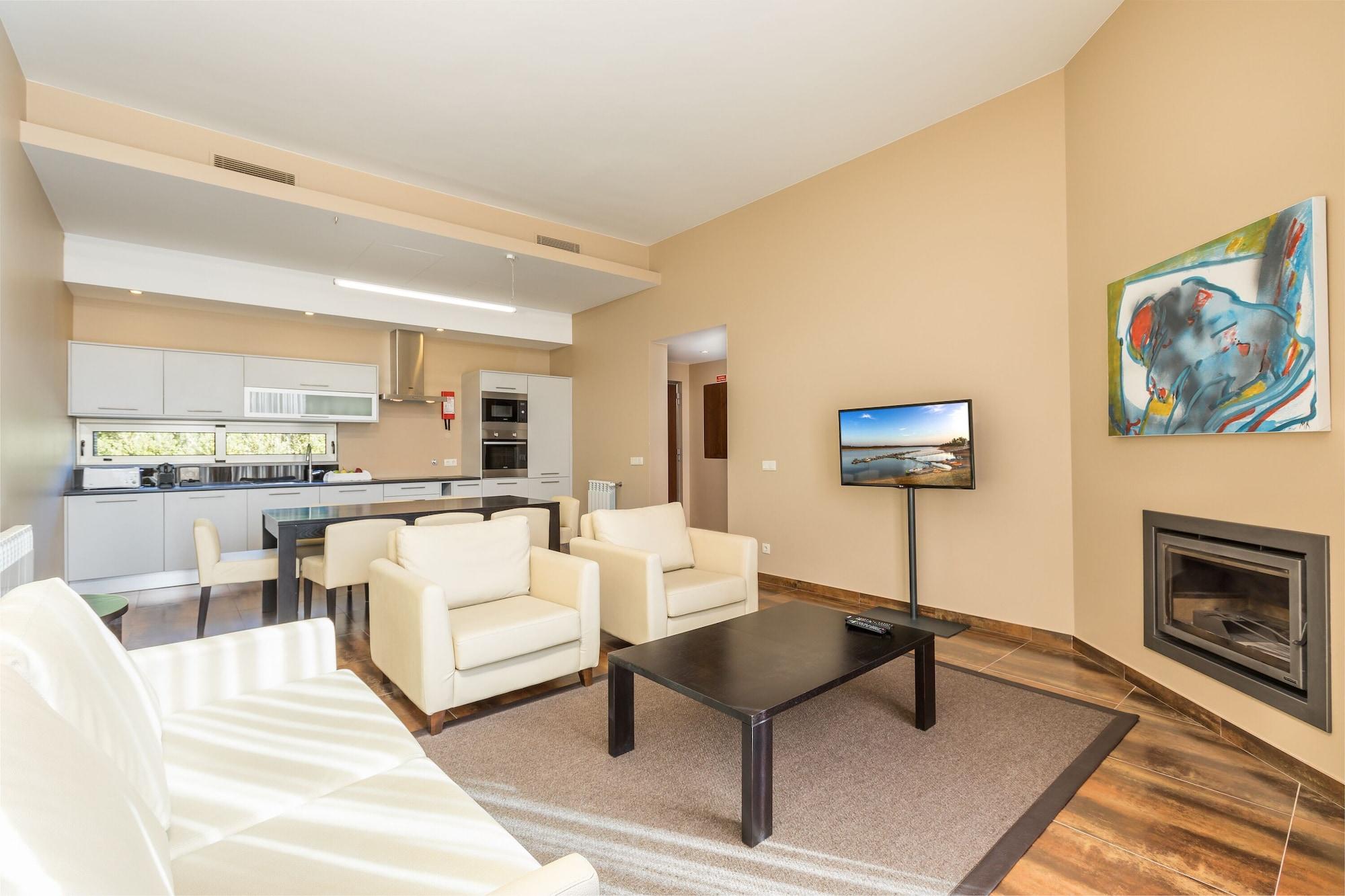 Ap Lago Montargil - Conference & Spa Buitenkant foto The photo shows a modern, spacious living area with a contemporary design. The room features light-colored walls and wooden flooring. 

In the center, there is a black coffee table surrounded by four white armchairs. A flat-screen TV is mounted on th