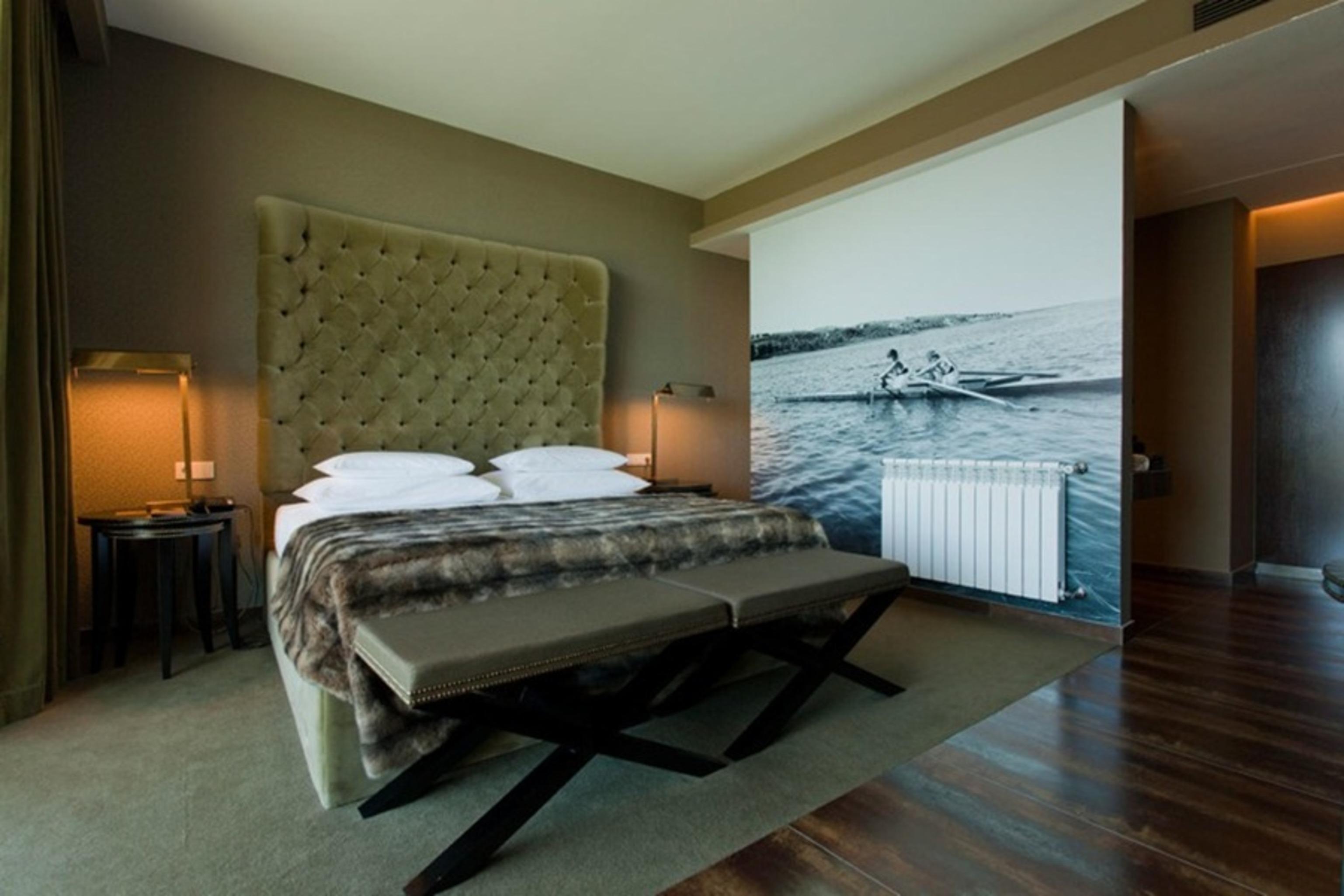 Ap Lago Montargil - Conference & Spa Buitenkant foto The photo shows a modern hotel room featuring a large bed with a tufted headboard and plush bedding. The color palette is neutral, with shades of green and gray. On one side of the room, there are bedside tables with lamps. A comfortable bench sits a