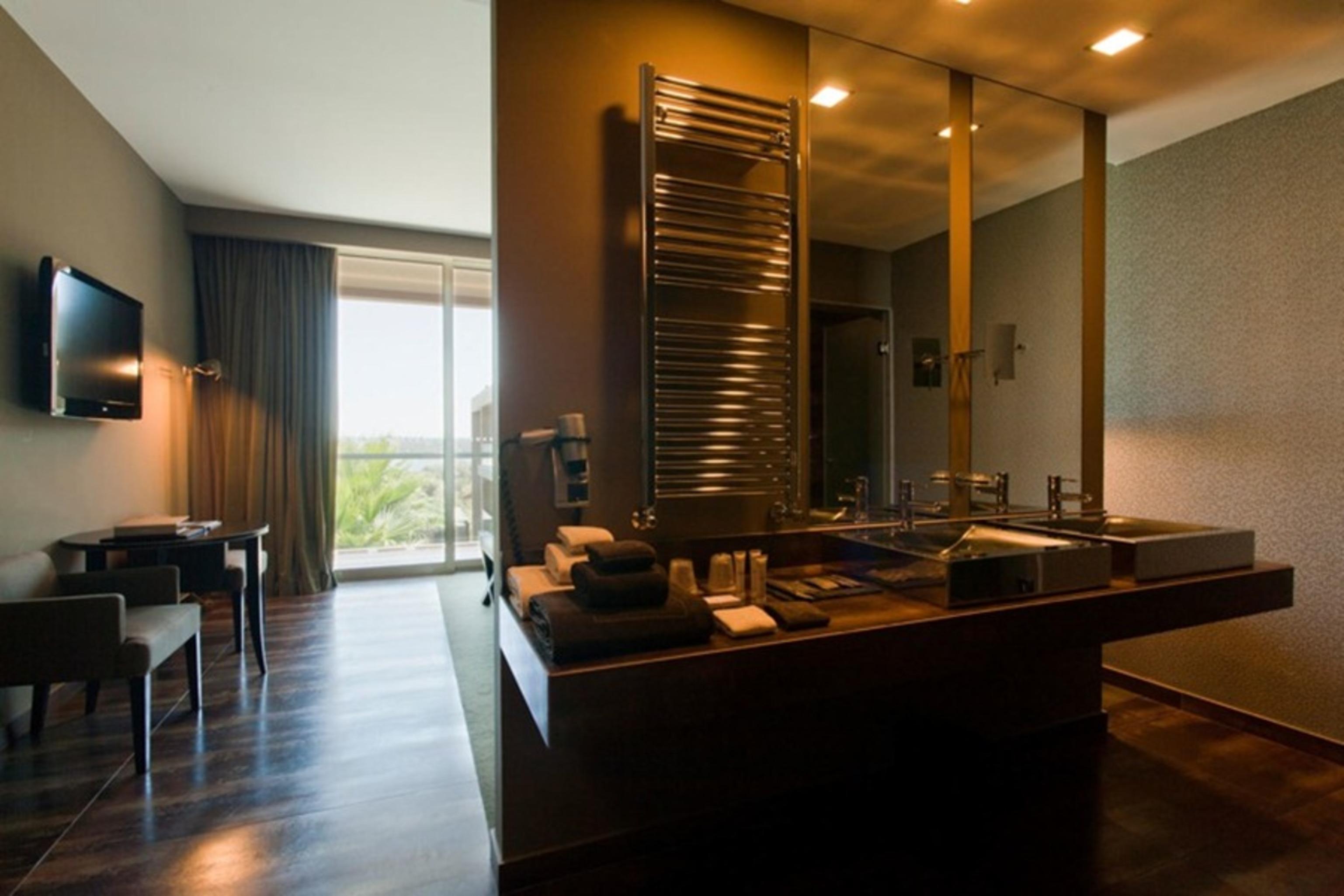 Ap Lago Montargil - Conference & Spa Buitenkant foto The photo displays a modern hotel room with a contemporary design. The room features a large window, allowing natural light to enter and offering a view outside. On one side, there is a sitting area with a small table and chairs. The other side showc