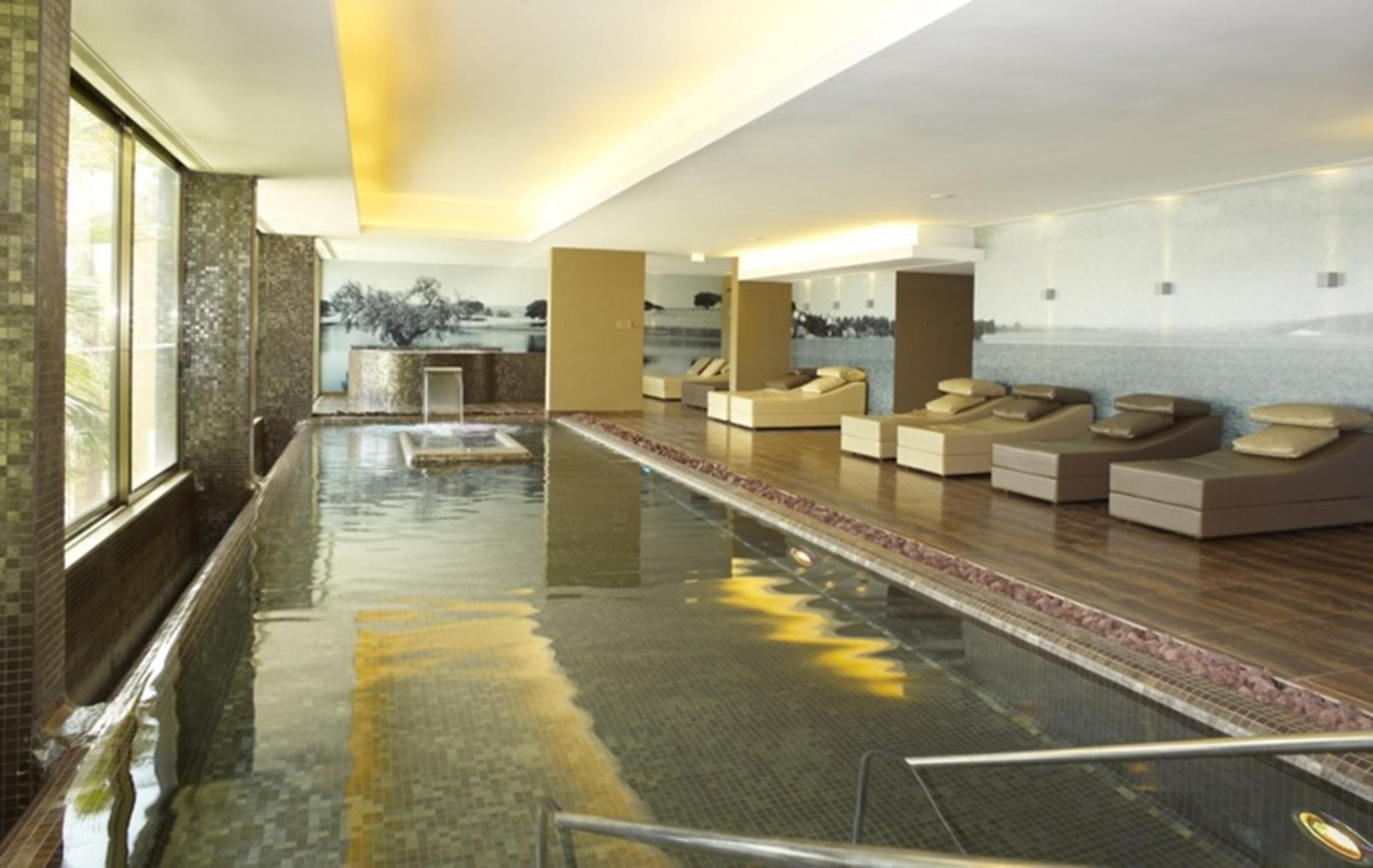 Ap Lago Montargil - Conference & Spa Buitenkant foto The photo shows a modern, serene spa environment. There is a swimming pool with calm water, reflecting the surrounding decor. Along the sides, there are several comfortable lounge chairs arranged, perfect for relaxation. Large windows allow natural l