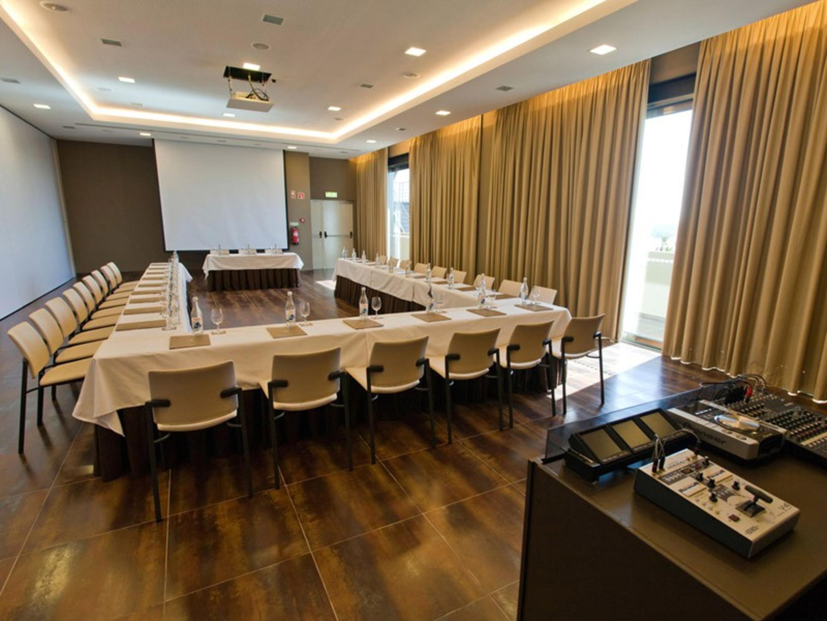 Ap Lago Montargil - Conference & Spa Buitenkant foto The photo shows a modern conference room set up for a meeting. There are several tables arranged in a U-shape, surrounded by chairs. A large screen and projector are positioned at the front, with a table for speakers or presenters. The room has large