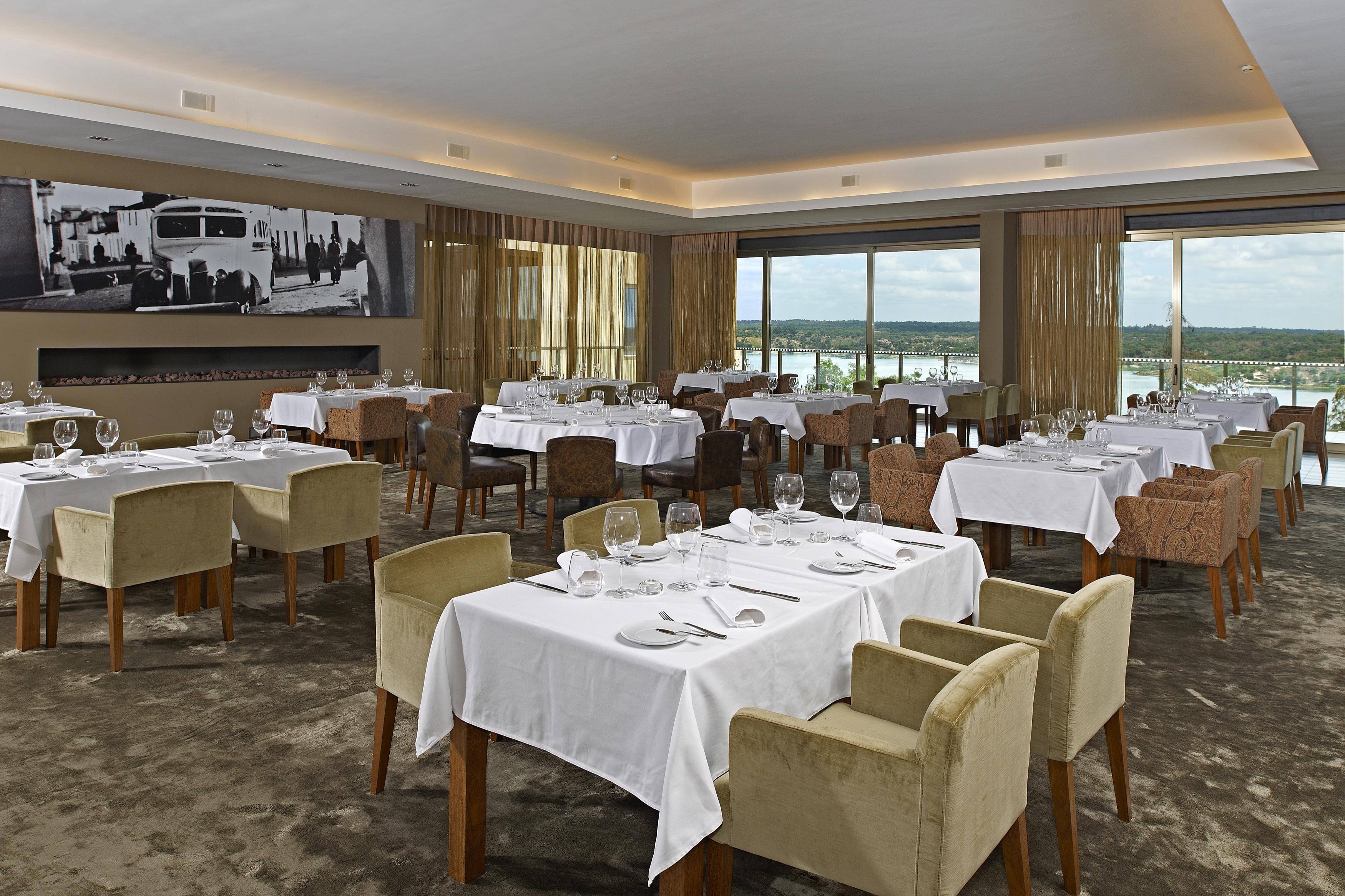 Ap Lago Montargil - Conference & Spa Buitenkant foto The photo shows an elegant restaurant interior featuring neatly arranged tables with white tablecloths. Each table is set with plates, cutlery, and glasses. The seating includes a mix of upholstered chairs in different colors—some light and others da