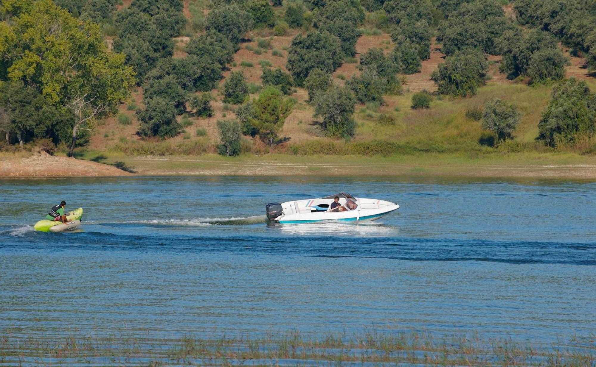 Ap Lago Montargil - Conference & Spa Buitenkant foto The photo shows a scene on a water body, likely a river or lake. In the foreground, a speedboat is moving quickly through the water, leaving a wake behind it. There are two people visible in the boat. In the background, there is a hilly area covered 